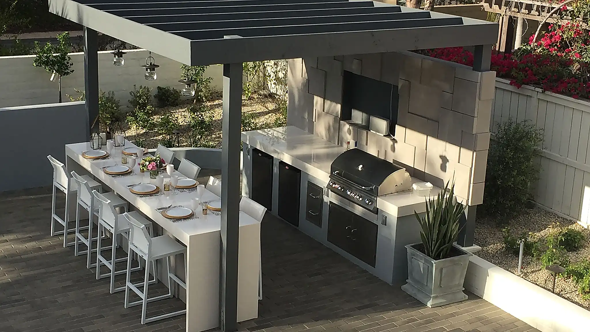 Outdoor kitchen and BBQ under a modern pergola with bar seating in a villa garden