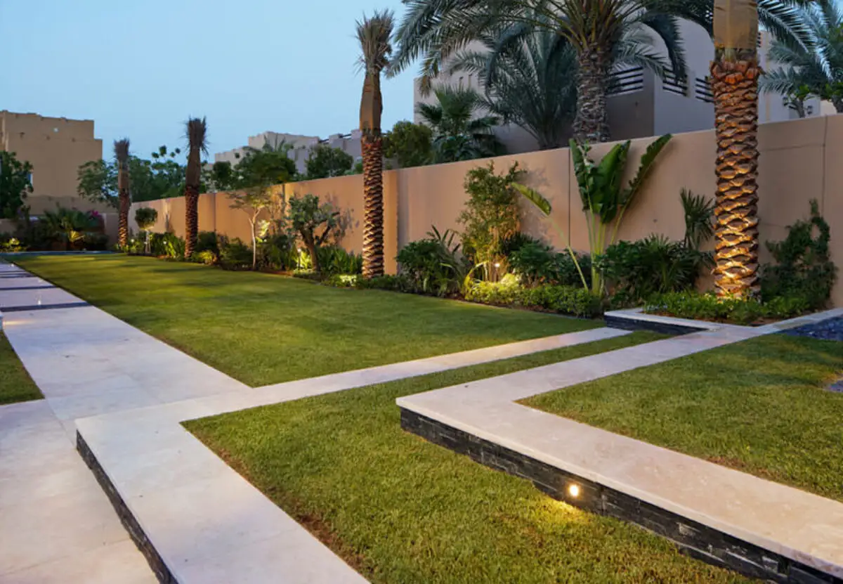 Contemporary resort style villa garden design in Dubai with palms, lawn, and warm landscape lighting